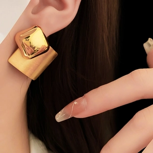 Detail showing gold geometric square and brushed rectangle earrings on model ear