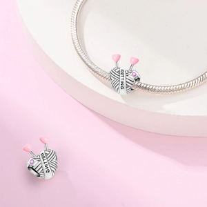 Macro view of silver knitting ball charm with pink heart needles and engraving