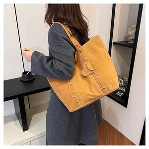 Detail of yellow suede tote bag featuring silver studs and heart-shaped metal decoration