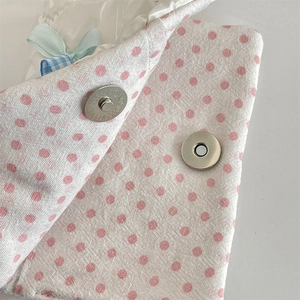 Macro detail of white polka dot passport holder with silver magnetic snap and blue bow