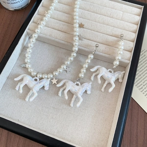 Détail du collier de perles et boucles d'oreilles licorne dans un écrin en velours beige