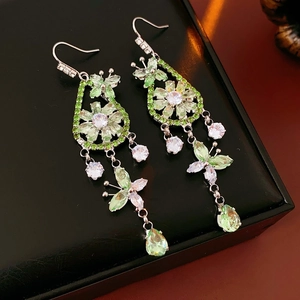 Zircon butterfly flower drop earrings with green stones on a black leather surface
