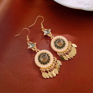 Détail de boucles d'oreilles bohèmes avec feuilles dorées, pierre et perles