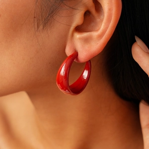 Close-up of a wide red acrylic hoop earring worn by a model with a glossy finish