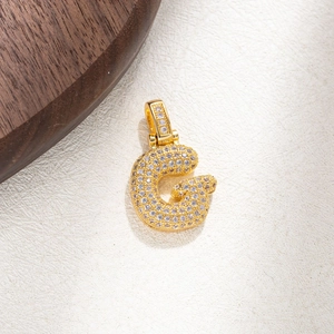 Macro shot of gold-plated letter G pendant with micro-pave zircons on textured surface