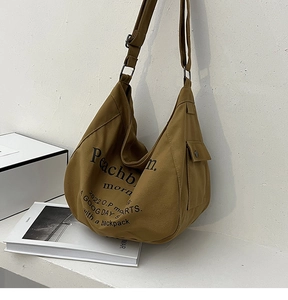 Détail du sac cabas en toile montrant la poche latérale à rabat et l'imprimé de lettres