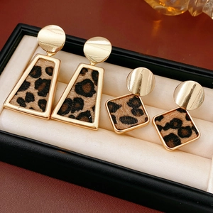 Détail de boucles d'oreilles léopard en formes trapèze et losange sur un coussin