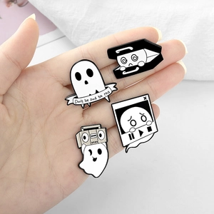 Detailed close-up of cartoon ghost enamel pins with music and coffin motifs on hand