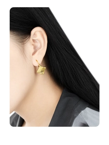 Detailed view of square gold stud earring with lava texture and diamond on ear