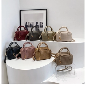 Detailed view of woven Boston bags in eight elegant colors on a white display stand