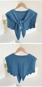 Detail of blue knit shawl featuring hollow diamond patterns and wavy hem on a hanger