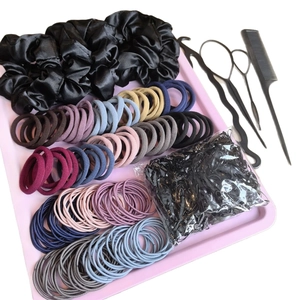 Satin scrunchies and colorful elastic hair ties set with styling tools on pink tray