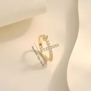 Adjustable golden cross ring with pavé crystals and central diamond on beige background