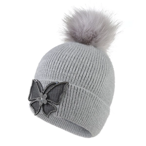 Detail of grey winter knit beanie featuring a fluffy pompom and rhinestone butterfly accent