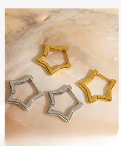 Macro shot of gold and silver star hoop earrings displayed on a glossy pearl shell base