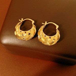 Detail view of gold U-shaped woven earrings on a brown leather jewelry box display