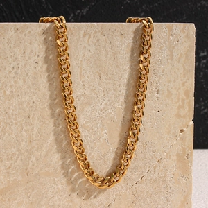 Detail of chunky gold chain necklace hanging on beige marble block with shadow play