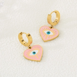 Détail de boucles d'oreilles créoles dorées avec coeurs roses et motif œil protecteur