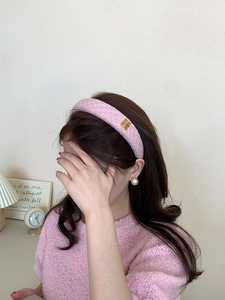 Primo piano di un cerchietto in tweed rosa con logo dorato indossato da modella