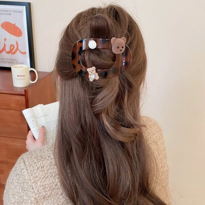 Close-up of a tortoiseshell hair claw with a small brown bear and pearl on wavy hair