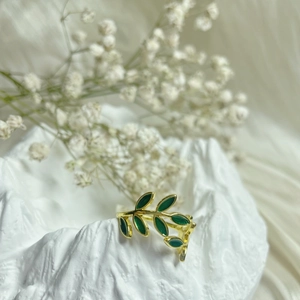 Elegant gold-tone open leaf ring with green enamel finish on a white textured stand