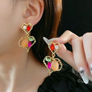 Dettaglio di orecchini vintage a cuore dorati con strass colorati su una modella