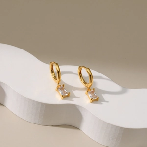 Gold plated hoop earrings with rectangular zircon drops on a white display stand