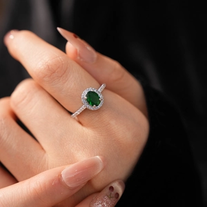 Macro shot of an oval green gemstone ring with pavé diamonds worn on a finger