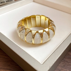 Detail of gold metal and white marble resin stretch bracelet inside a gray jewelry box