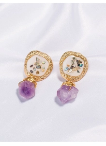 Detail of gold shell earrings with purple gemstone hanging on white satin fabric