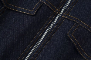 Vue détaillée du tissu denim bleu foncé avec coutures jaunes et fermeture éclair en métal