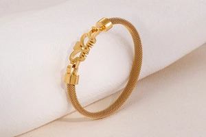 Close-up of gold mesh bracelet featuring MOM letter heart charm on textured fabric