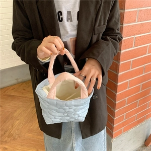 Close-up of a light blue quilted mini bag with pink handles on a wooden floor