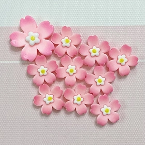 Flat lay of ten cherry blossom resin charms with pink white gradient petals and yellow stamens