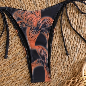Detail of black bikini bottoms with orange tiger lily print and side ties on straw mat