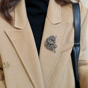 Detailed close-up of a hollow horse brooch with silver finish on a camel coat lapel