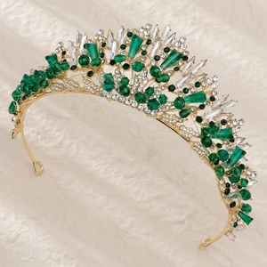 Close-up of gold crown featuring green crystals and white rhinestones on white fabric