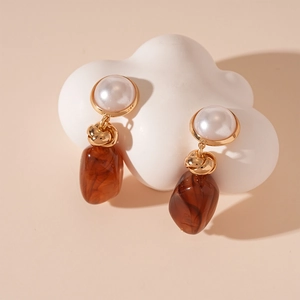 Detail view of brown resin earrings with faux pearls and gold accents on a white stone