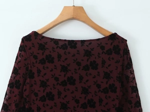 Detail of burgundy sheer mesh top with black flocked floral pattern on a wooden hanger