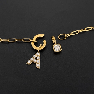 Dettaglio macro collana in acciaio titanio dorato con lettera A di perle e zircone quadrato