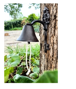 Close-up of vintage cast iron door bell with key motif and braided rope on tree trunk