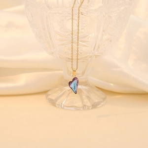Macro detail of a heart-shaped purple crystal pendant with a gold chain on silk