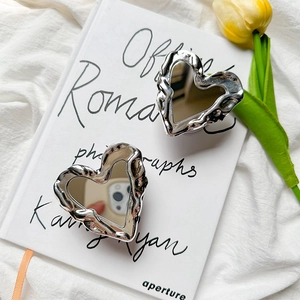 Detail of two silver heart-shaped mirror phone grips on a white book with a tulip