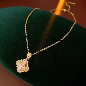 Détail d'un collier trèfle doré avec perles et pierres sur un coussin en velours
