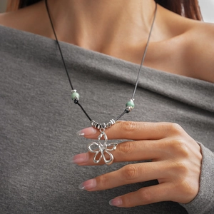 Gros plan d'un pendentif fleur argenté sur un collier cordon noir avec des perles vertes