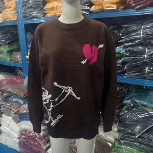 Dettaglio di un maglione marrone in maglia con cuore rosa e grafica bianca di Cupido