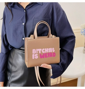 Detail view of tan crossbody bag with pink artistic slogan print and top handle
