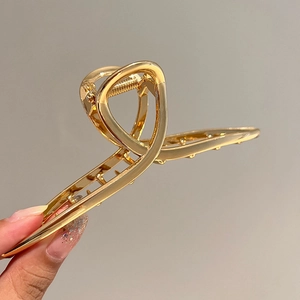 Close-up of a large gold metal hair claw clip with a twisted hollow design held by hand