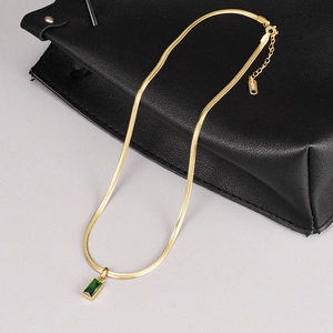 Macro detail of K18 hallmark on golden snake chain with emerald zircon pendant