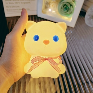 Detail shot of a glowing teddy bear night light with pink plaid ribbon and warm LED light